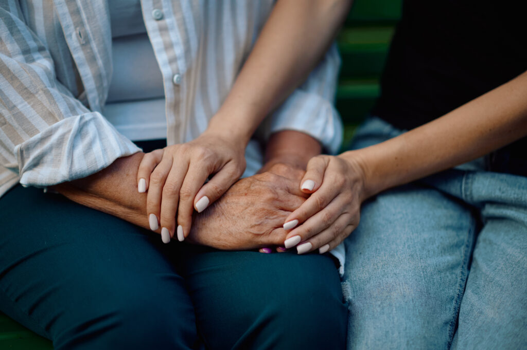 Close-up of a younger person holding the hands of an elderly individual in a comforting gesture